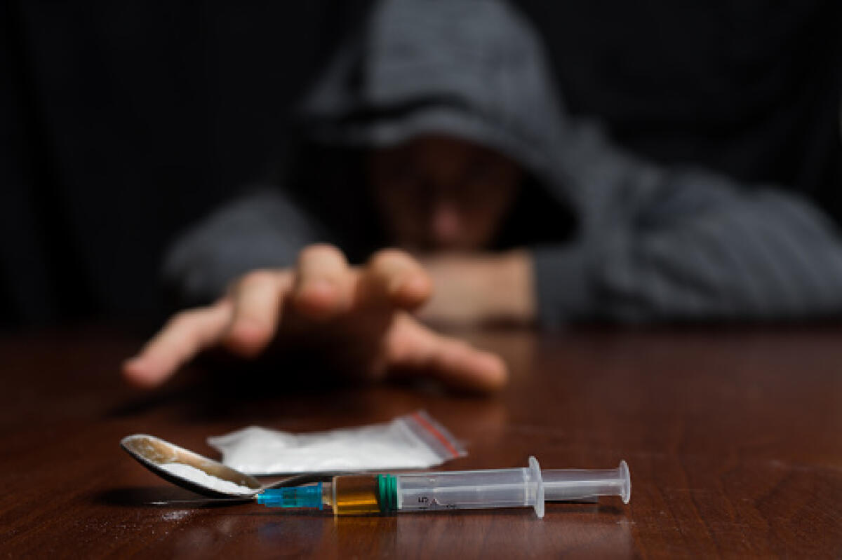 XXXIII Giornata Internazionale contro l’Abuso di Droghe e il Traffico Illecito - Addict at the table pulls his hand to the syringe with the dose. Copy paste