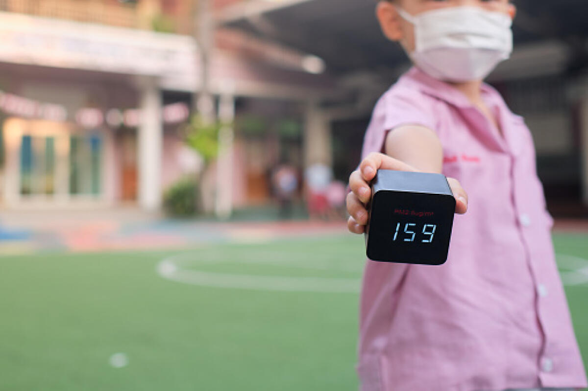 Scuola e Salute: perchè l’aria salubre nelle aule è la nostra “Mission” - Little Asian kindergarten student boy with respirator mask for protection holds PM2.5 Air Quality Monitor / Detector ,show hazardous high level of dust & air pollution at school yard, PM 2.5 concept