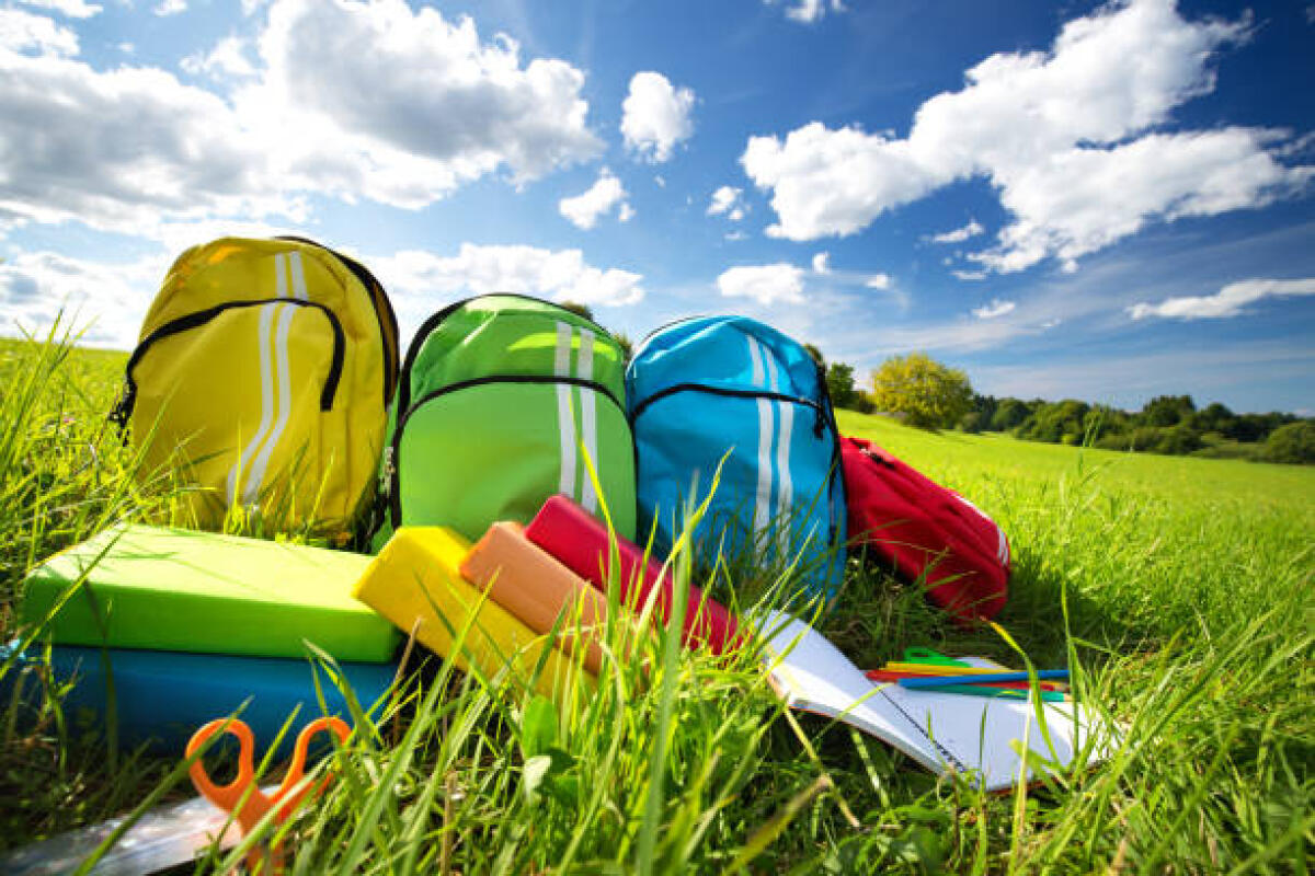 Le uscite didattiche rivestono una funzione molto significativa all’interno di una progettazione didattica per una classe - Colourful children schoolbags outdoors on the field. Backpacks with school accessories