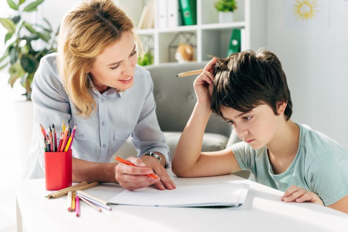 NOVAKID: Quali sono le sfide di apprendimento nell'infanzia e come superarle? - kid with dyslexia and smiling child psychologist sitting at table and holding pencils