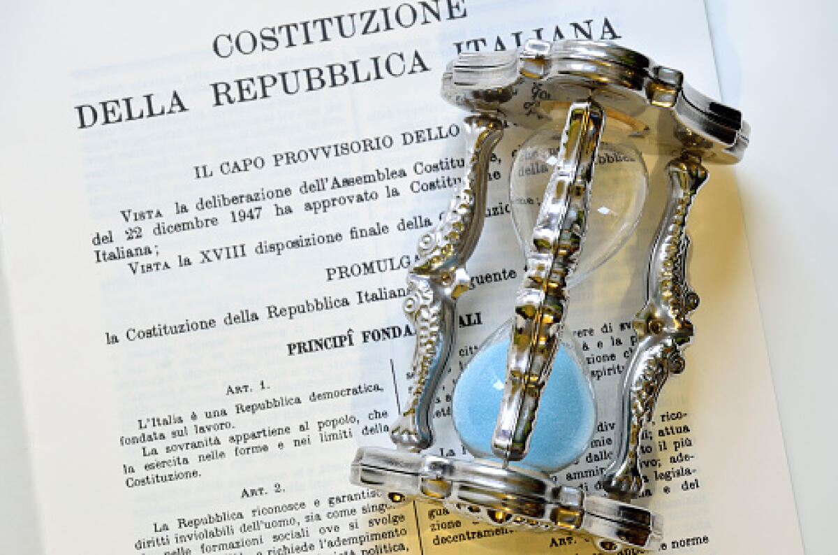 Scuola italiana, tra caos quotidiano e attese pasquali: concorsi sbagliati, precari stanchi e un sistema che cerca respiro - text of the Italian constitution with a silver hourglass with blue sand on it