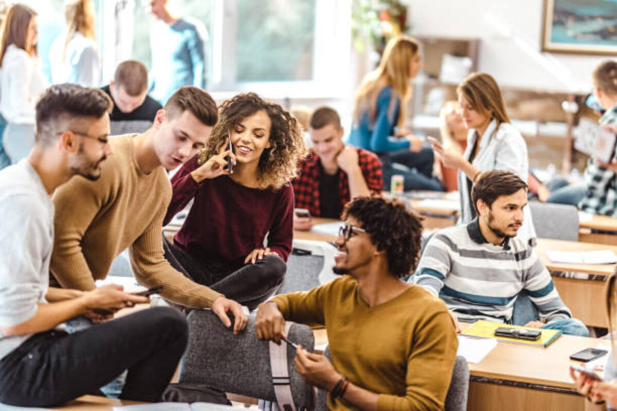 Cronache di una maturanda: Cosa succede nelle classi ad un mese dalla prova? - Large group of happy college students communicating during a break in the classroom. Focus is on woman talking on cell phone.